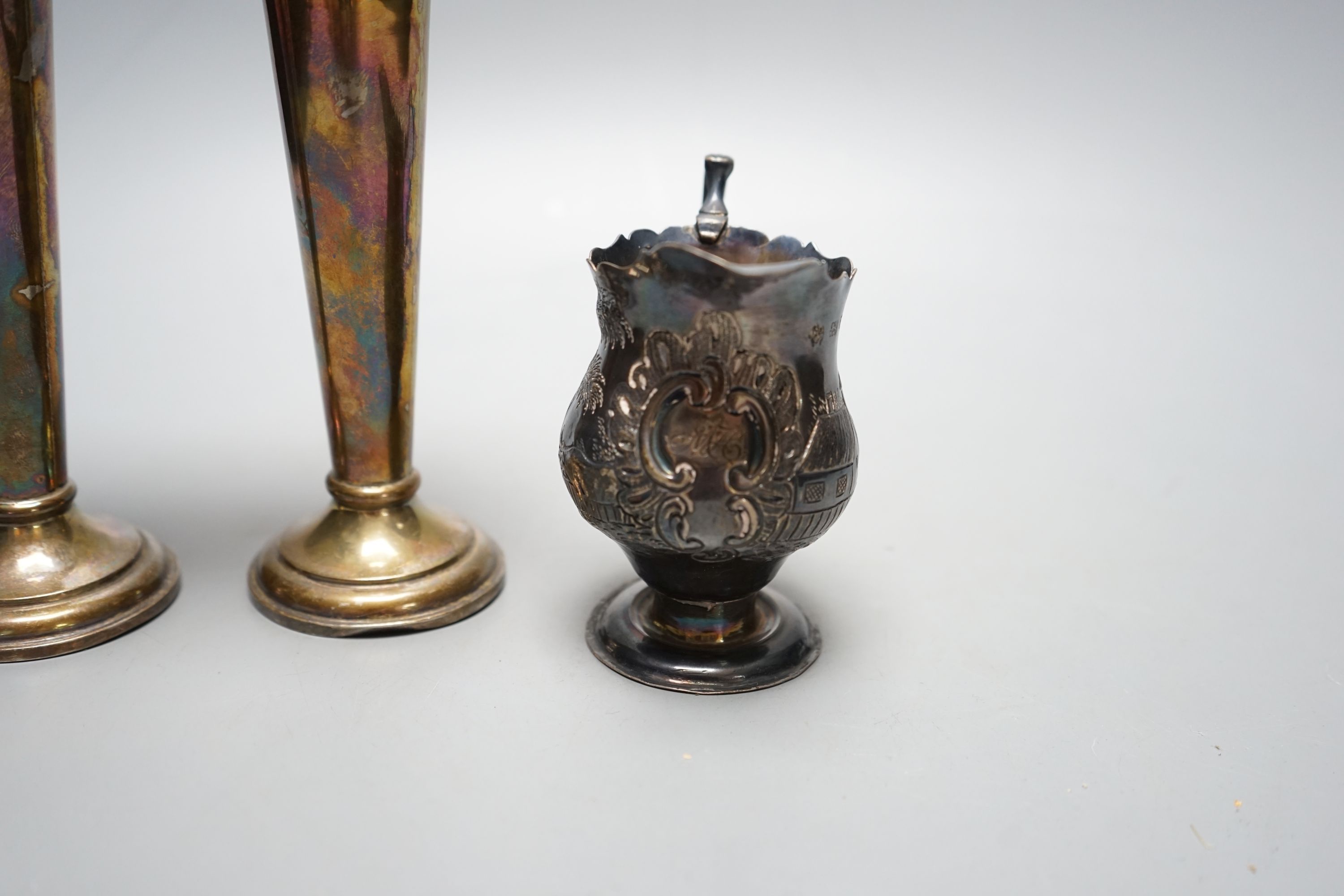 A George III silver helmet shaped cream jug, with later embossed decoration, London, 1759, 97mm and a pair of Edwardian silver spill vases, 16.3cm.